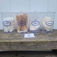 Front view of all four clear plastic medical canisters labeled Cotton, Tongue Depressors, Gauze, and Bandages filled with respective supplies