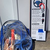 Photo showing the blue vinyl bag holding the coiled jumper cables along with the steering wheel lock cable packaging showing instructions for installation and removal.
