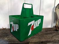 Side angle showing green plastic 7UP carrier with large white and orange logo on one side and handle visible