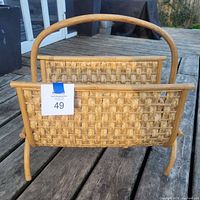 Front view of vintage rattan woven magazine rack showing basket weave pattern, wooden frame, and handle.