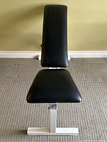 Front view of the adjustable weight bench showing black padded seat and backrest on white frame.