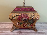 Front view of the floral ceramic box highlighting the detailed flower painting on gold background and claw feet.