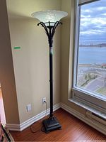 Full view of the torchiere floor lamp showing its height and design by a window.
