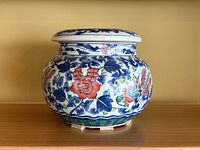 Front view of blue and white ceramic ginger jar with pink floral designs and bird motifs on wooden surface.