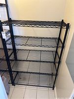 Photo showing the full 5-tier black metal shelving unit in a corner, highlighting the wire grid shelves and metal frame.