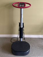 Front view of the Body Vibe Exercise Machine showing the round platform, central support pole with control panel, pink circular handlebar, and attached resistance bands.