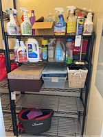 Cleaning supplies including sprays, liquids, and storage boxes on black metal shelving.
