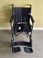 Front view of the wheelchair showing padded armrests, black upholstery, and footrests.