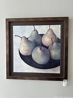 Framed modern wall art of five green pears in a black bowl, showing soft natural light and a dark wood frame.