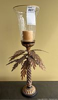Full view of metal palm tree candleholder with etched glass hurricane shade and candle inside.