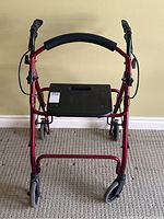 Front view of the red folding mobility walker showing black seat, padded grip, hand brakes and caster wheels