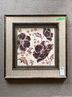 Framed floral art print showing three large dark brown flowers with smaller flowers and leaves on light background.