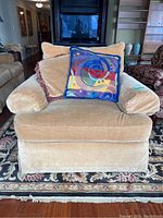 Front view of the oversized beige velvet lounge chair with three pillows on it, showing the plush cushions and fabric texture.