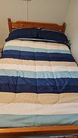 Full view of comforter on bed showing striped pattern in blue, beige, and cream colors.