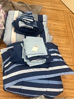 Two queen bedding sets with pillow covers laid out on wooden floor, showing striped blue and white design.