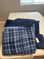 Folded queen size blue plaid comforter with solid dark blue pillow covers and bedding sheets on mattress.