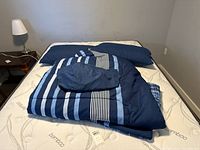 Photo of bed with folded striped navy blue blanket, two pillows, and sheets on a mattress.