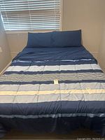 Full view of the queen size bed made with the striped comforter and two matching navy pillowcases.