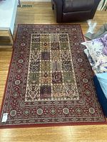 Full view of rectangular red carpet on wooden floor next to leather chair and table.