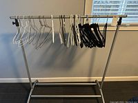 Full view of metal clothes rack with white, black plastic hangers and silver wire hangers on the horizontal bar