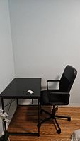 Desk and chair side view showing black desk surface and chair with arm rests and wheels