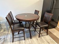 View of round wood dining table with four matching chairs in kitchen area, showing dark brown finish and upholstery.