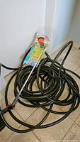 Coiled green garden hose with frost proof wand and spray nozzle attached, showing length and type of hose.