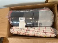 Box containing new bedding set, including a dark-colored microfiber comforter in packaging and red and white checkered sheets in packaging.