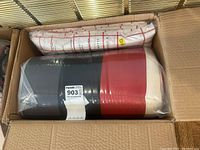 Top view of microfibre bedding pieces including one white-and-red checkered piece and one multi-colored comforter wrapped in plastic inside a cardboard box.