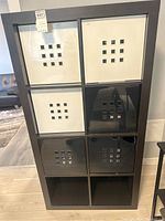 Full view of shelving unit showing 8 compartments and 4 decorative storage containers (2 white, 2 black). One black container is visibly cracked.