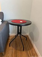 Side view of black metal side table positioned next to a grey upholstered sofa showcasing its tripod leg base and round top.