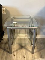 Front view of the metal and glass side table showing the clear glass top and metal frame.