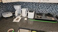 Overview of lot on kitchen countertop showing sandwich maker, coffee maker, kettle, toaster, and hot plate.