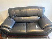 Front view of black pleather sofa showing cushioned back, armrests, and seating surface.