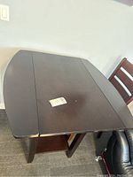 Table with foldable sides in dark wood finish, visible scratches on top surface, chair partially visible
