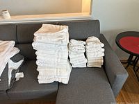 White hand and bath towels stacked on gray couch from an angle showing multiple piles.