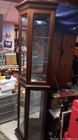 Front and side view of the tall wooden framed curio cabinet with glass sides and shelves, showing overall condition and design.