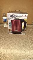 Front view of the Americana Electric Kettle box placed on a beige surface, water bottle visible for size comparison.