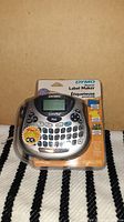 Front view of the DYMO LetraTag personal label maker in sealed original packaging with visible keyboard, LCD screen, and branding.
