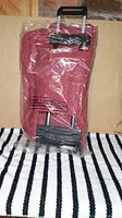 Red soft fabric wheel luggage in clear plastic wrapping, shows retractable handle and wheels.