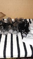 Photo of 8 black LED garden spotlights, each individually wrapped in protective plastic, arranged on a striped fabric background. One instruction sheet and remote control also visible.