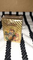 Sealed Pokémon booster box wrapped in gold plastic with Ash Ketchum and Pikachu artwork on front.