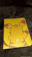 Front view of yellow trading card binder with Pikachu design showing minor discoloration spot on backing.