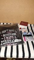 Photo showing black folded sweatshirt with slogan in packaging, jewelry cleaner box, and travel bag set on striped background.