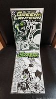 Photo of two Green Lantern Rebirth comic book variants, issues 1 and 2, displayed against a black background. Both comics feature black and white cover art in near mint condition.