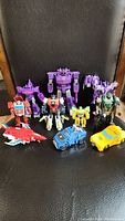 Nine Transformers figures on a black chair, assorted Autobots and Decepticons in various colors and sizes