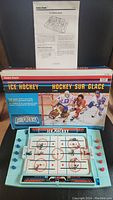 Photo showing game set up with ice rink playing surface, nets at each end, and original box behind the game. Instruction sheet visible.