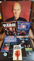 Photo of Star Trek Captain Jean-Luc Picard poster, several Star Trek magazines and books, and Star Trek model pieces.