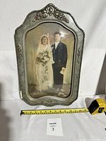 Full view of antique wedding photo in ornate curved metal frame with convex bubble glass. Tape measure visible for size reference.