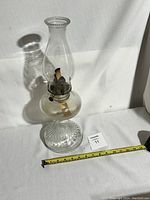 Side view of the antique Queen Mary oil lamp showing ribbed glass base, round reservoir, metal burner with wick, and clear chimney with beaded edge.